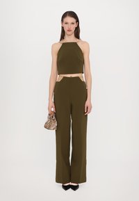 Top scurt de culoare verde măsliniu cu bretele din lanț, asortat cu pantaloni cu talie înaltă și accente laterale bej. Accesoriu: geantă cu model.