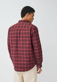 Rot- und schwarz-karierter Hemd mit langen Ärmeln, Button-Down-Kragen und leicht abgerundetem Saum. Verfügt über eine einzelne Rückenpasse und Knopfmanschetten.