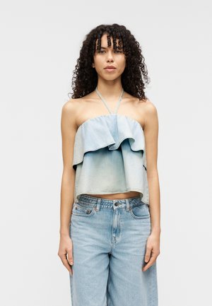 Hellblaues bauchfreies Oberteil aus Denim mit einem mehrlagigen Rüschendesign. Kombiniert mit hoch taillierter hellblauer Jeans.