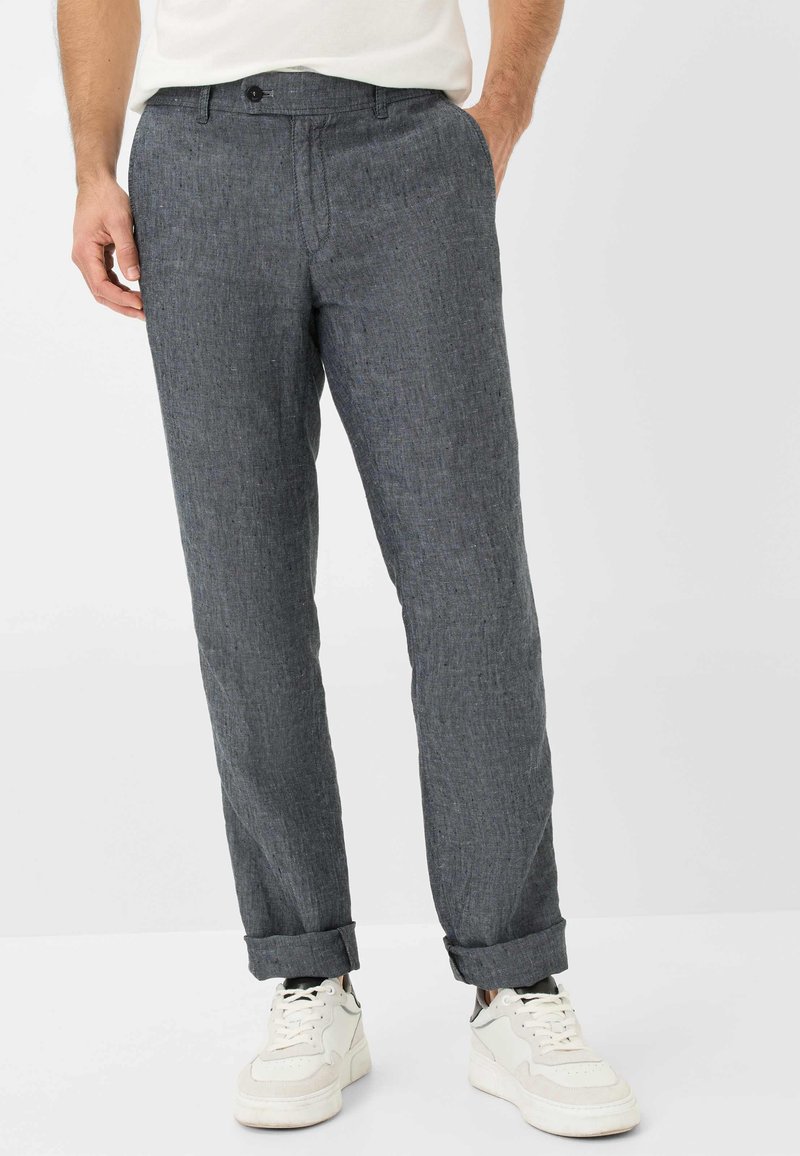 Pantaloni grigi in misto lino per uomo con una finitura testurizzata, forma affusolata, piega singola e orli con risvolto, abbinati a sneakers bianche.