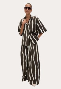 Ensemble deux pièces rayé marron et blanc, comprenant une chemise à manches courtes ample et un pantalon large. Tissu lisse ; accents soignés.
