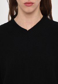 Fekete kötött pulóver mély V-nyakkivágással és bordás gallérral, texturált anyagból és laza szabással.