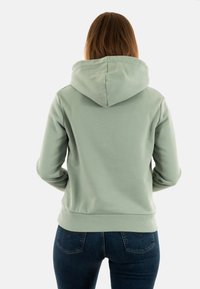 Mintgroene hoodie met een trekkoordcapuchon en geribbelde mouwen. De achterkant heeft een gladde textuur en is gecombineerd met blauwe spijkerbroeken.