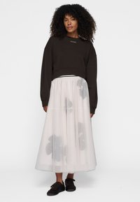 Brun cropped sweatshirt, gennemsigtig hvid tylnederdel med blomstermønster og sorte sko. Afslappet pasform, lange ærmer og tekstureret stof.