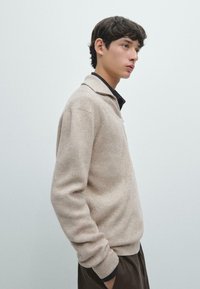 Maglione beige a coste con scollo con colletto, maniche lunghe e vestibilità comoda. Tessuto texturizzato con una leggera lucentezza.