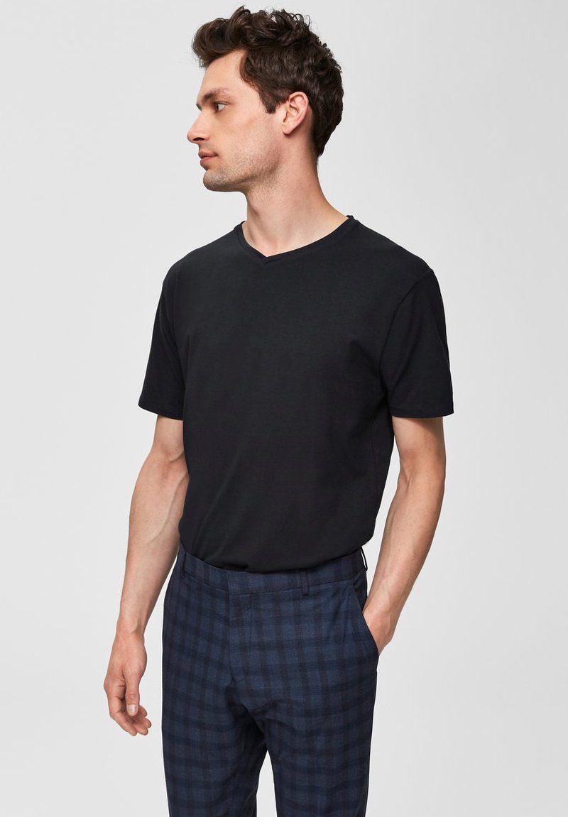 Camiseta negra de cuello en V y mangas cortas, combinada con pantalones de cuadros azul oscuro que presentan un sutil patrón de cuadros y bolsillos frontales planos.