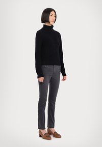 Schwarzer gerippter Rollkragenpullover, kombiniert mit dunkelgrauen Slim-Fit-Jeans und braunen Blockabsatzschuhen mit einem dekorativen Akzent nahe der Spitze.