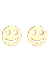 Złote metalowe kolczyki w kształcie uśmiechniętych twarzy z wyciętymi oczami i ustami, o gładkim, błyszczącym wykończeniu.