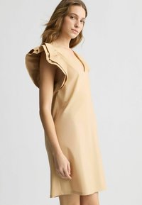 Abito beige con scollo a V e maniche a ruffles, realizzato in tessuto morbido. Il design è dritto, fino al ginocchio, con dettagli minimi.