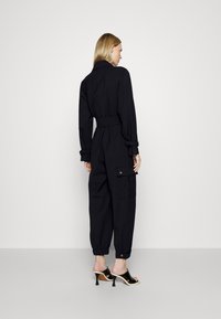 Mono negro con cintura ajustada, bolsillos tipo cargo, mangas largas y tobillos ceñidos. Tejido suave con un corte entallado.