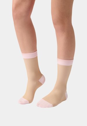 Legs wearing beige ribbed socks with light pink cuffs, heels, and toes against a plain light background.