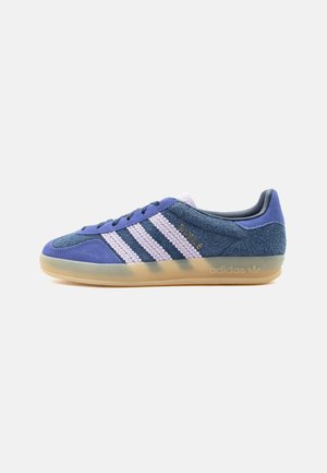 Lavtopet sneaker i blå ruskind med hvide teksturerede striber, gennemsigtig gummisål og gyldent "BAYRE" branding på siden.