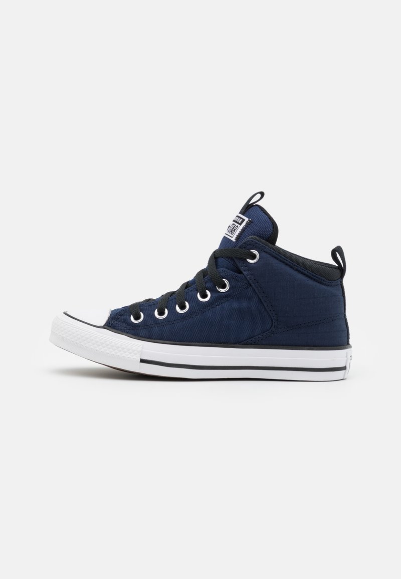 Baskets montantes bleu marine avec semelle en caoutchouc blanche, lacets noirs, œillets métalliques et écusson blanc avec logo sur la languette.