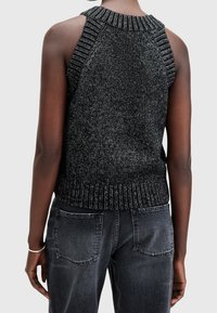 Svart stickad linne med ribbad halsringning och ärmhål, med ett mönstrat textur. Kombinerad med mörka jeans i denim, visad bakifrån.