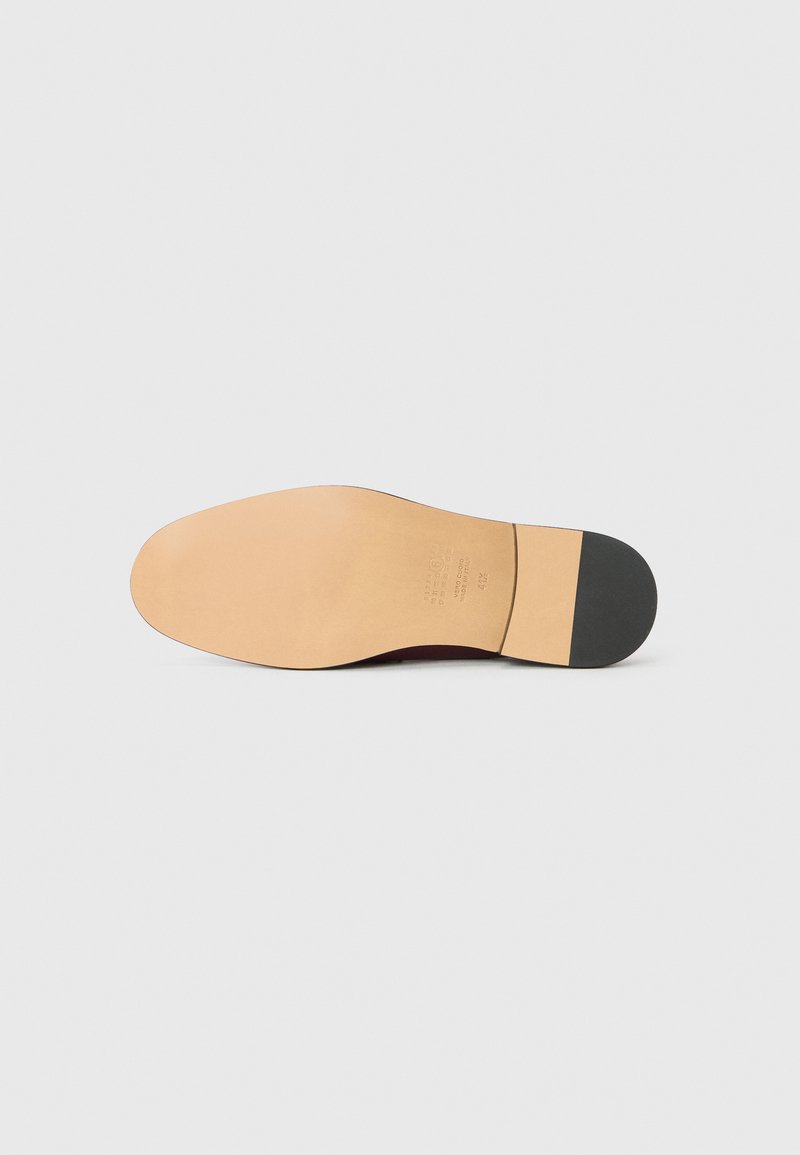 Leather shoe sole with a smooth beige finish, featuring a rounded shape, a slight heel, and a black rubber accent at the heel's edge.