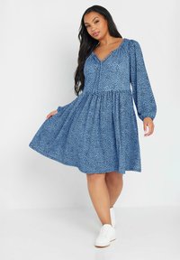 Niebieska sukienka z wzorzystą teksturą, długimi puffami, dekoltem w kształcie litery V, marszczoną talią i rozszerzonym dołem. Noszona z białymi sneakersami.