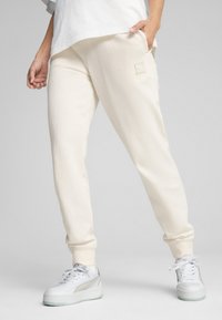 Pantaloni della tuta color crema in tessuto morbido con una vestibilità rilassata, dotati di una piccola etichetta logo sulla coscia e polsini elasticizzati.