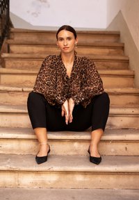 Leopard print blouse, black pants, black flats; sitting on stone stairs. Features medium-length sleeves, button details, and sleek design.