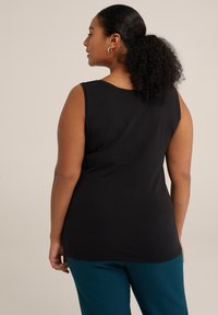Top negro sin mangas hecho de tela suave, con un escote redondeado y un corte relajado, combinado con pantalones en color teal.