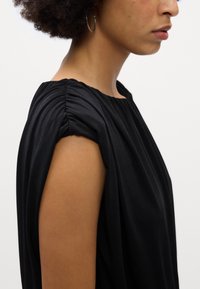 Top preto sem mangas com um design franzido nos ombros. Textura suave com um corte solto e um decote largo.
