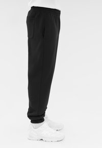 Zwarte jogpants met een relaxte pasvorm, elastische tailleband, zijzakken en geribbelde boorden, gecombineerd met witte sportschoenen.