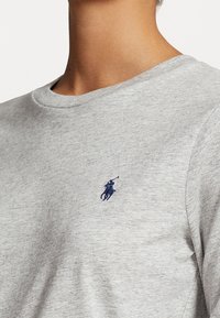 T-shirt in cotone grigio chiaro con scollo a girocollo, maniche corte e logo ricamato blu navy sul petto. Texture liscia.