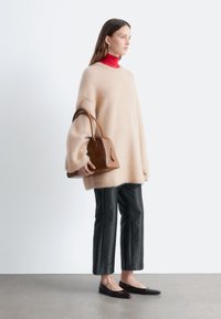 Beiger flauschiger Oversize-Pullover, roter Rollkragenpullover, schwarze kurze Hosen, braune strukturierte Handtasche, schwarze spitze Ballerinas, minimalistische Umgebung.