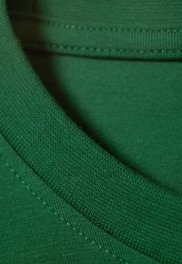 Tessuto di t-shirt in cotone verde con colletto a girocollo a costine. Presenta una fine trama e dettagli di cucitura lungo il colletto e la cucitura del corpo.
