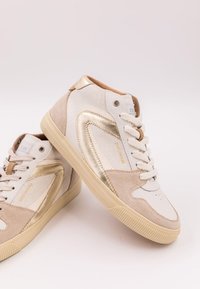 Höga sneakers i vitt läder, beige mocka och gyllene metalliska detaljer. Har snören, perforerat tåparti och strukturerade sidopaneler.