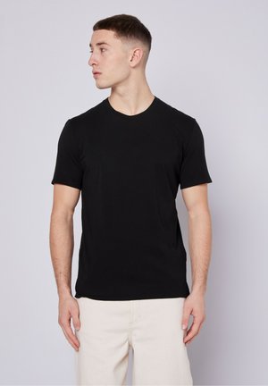 Black short-sleeve T-shirt with a crew neckline, made of soft fabric, features a fitted shape and smooth texture, worn with beige pants.