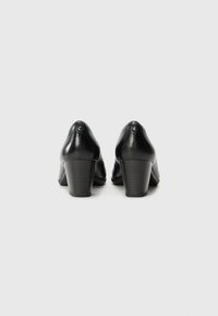 Black leather heels with a curved design, moderate block heel, smooth texture, and subtle button detail at the back.