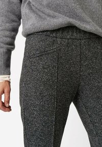Szare spodnie z mieszanki wełny o teksturowanym wzorze jodełki, z bocznymi kieszeniami i dopasowanym krojem. Rękaw swetra częściowo widoczny na górze.