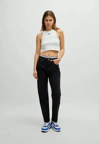 Top halter branco com nervuras combinado com calças pretas de cintura alta, apresentando um cós com detalhes em azul, e ténis azuis e brancos.