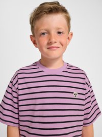 Junger Junge mit kurzen hellbraunen Haaren, der ein lila-schwarzes gestreiftes T-Shirt mit einem Bienenlogo auf der Brust trägt und leicht lächelt vor einem einfachen Hintergrund.