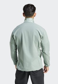 Chaqueta de concha suave en verde claro, con un cuello alto, hombros texturizados y costuras anguladas, que presenta un acabado suave y una silueta elegante.
