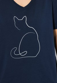 Námořnická modrá tričko s výstřihem do V vyrobené z měkké tkaniny, která na přední straně obsahuje bílý obrys sedící kočky v minimalistickém designu.