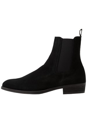 Zwarte nubuck Chelsea-boot met elastische zijpanelen, ronde neus, lage gestapelde hak en een handvat aan de achterkant voor gemakkelijk aan- en uittrekken.