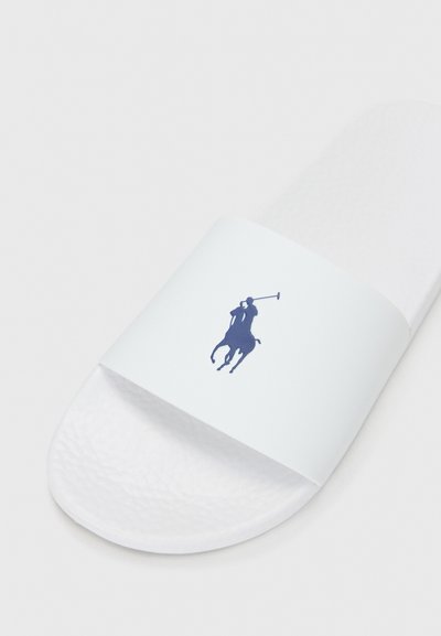 Vit slip-on sandal med en texturerad sula och en bred rem med en marinblå polo-spelare logotyp. Slät yta, minimalistisk design.