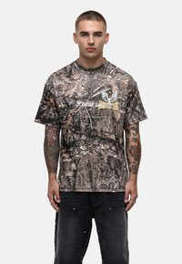 Koszulka w moro w odcieniach brązu i zieleni, okrągły dekolt, krótkie rękawy oraz nadruk logo z przodu w kolorze żółtym.