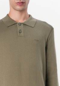 Langärmliges olivgrünes Poloshirt aus weichem Stoff, mit klassischem Kragen, zwei Knopf-Leiste und dezentem Logo-Stick.
