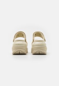 Crocs beige con finitura lucida, design posteriore con cinturini regolabili, fori rotondi e suola con battistrada testurizzato.
