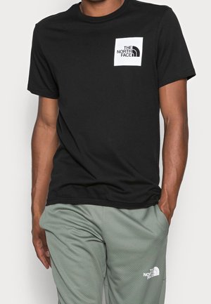 Homme portant un t-shirt noir The North Face et un pantalon vert clair avec le logo The North Face sur la cuisse.