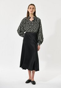 Črna dolga krila s tekočo silhueto, ki jo dopolnjuje črna in bela bluzica z vzorcem, ki ima gumbasto ovratnik in široke rokave.