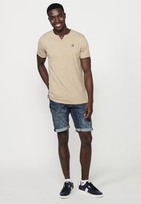 Beige, rövid ujjú, V-nyakú póló, hímzett logóval, kék farmer sorttal, which rolled hems and patch pockets.