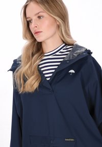 Sötétkék vízálló dzseki kapucnival, ezüst béléssel és kis esernyő logóval. Egyszerű kialakítás, patentos elülső zsebbel.