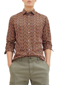 Bruine shirt met patroon, gekenmerkt door een mix van oranje, witte en blauwe vormen, met een knoopsluiting en lange mouwen, gedragen met groene broek.