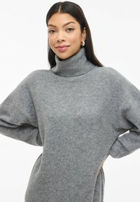 Maglione grigio a collo alto realizzato in morbido tessuto knit, con una vestibilità ampia, spalle abbassate e maniche lunghe. Texture liscia, senza motivi.
