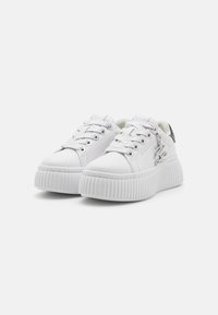 Weiße Sneakers mit einer strukturierten, dicken Plattformsohle, ausgestattet mit metallischen Ösen und Schnürsenkeln sowie einem glatten Obermaterial. Niedrig geschnittenes Design.