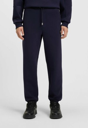 Navy blue sweatpants made of soft material; features an elastic waistband with a drawstring and side pockets. Worn with black sneakers.