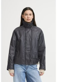 Svart lättviktsjacka med hög krage och tryckknappar. Har raglanärmar, texturerad tyg och framfickor. Stylen är ihop med blå jeans.